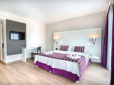 Modernes Hotelzimmer mit Doppelbett in Weiß und Lila, Schreibtisch und Wand-TV.