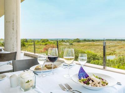 Tisch mit Wein und Salat auf Terrasse mit Blick auf Wiesen und blauen Himmel.