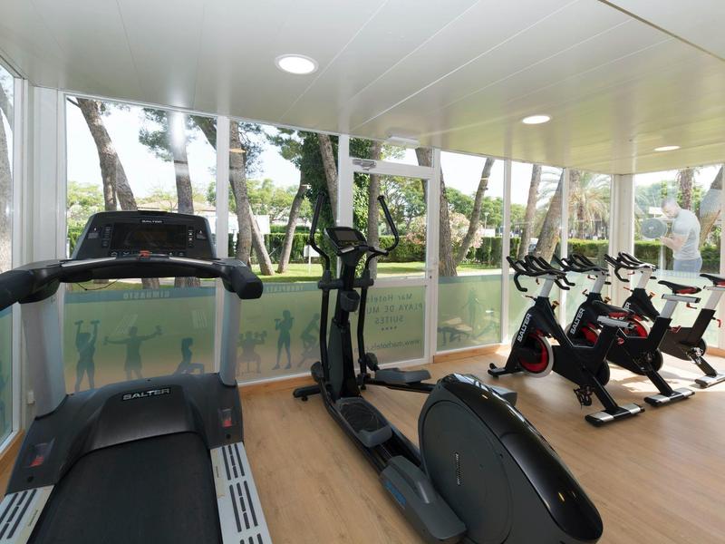 Moderner Fitnessraum mit Laufband, Crosstrainer und Spinning-Bikes und großen Fenstern.