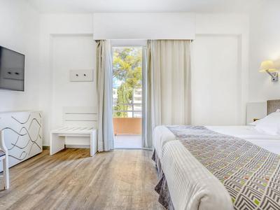 Helles Hotelzimmer mit Doppelbett, Holzboden und Balkon mit Blick auf Bäume.