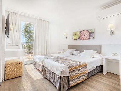 Helles Hotelzimmer mit zwei Einzelbetten, Holzboden und Balkon mit Meerblick.