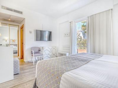 Camera d'hotel luminosa con biancheria da letto bianca, TV e accesso al balcone.