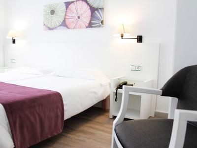 Modernes Hotelzimmer mit Doppelbett, weißer Bettwäsche und violettem Überwurf, Stühlen und Wandkunst.