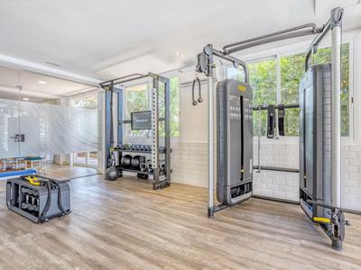 Modern gym with strength machines, dumbbell rack, and wood floor in bright room.