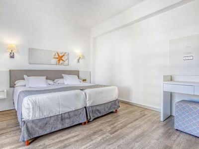 Lichte hotelkamer met twee bedden, houten vloer en modern bureau met kruk.