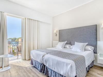 Lichte hotelkamer met twee eenpersoonsbedden, grijs hoofdeinde en balkon met uitzicht op de stad.