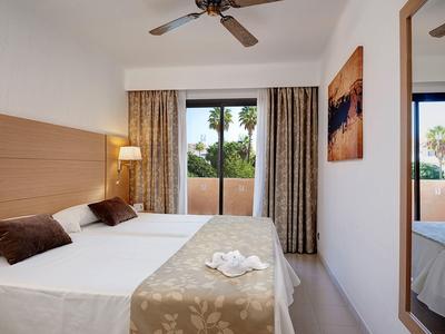 Lichte hotelkamer met tweepersoonsbed, balkon en plafondventilator.