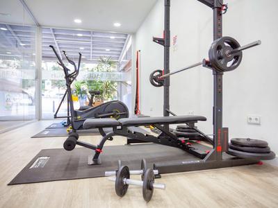 Fitnessraum mit Hantelbank, Langhantel, Kurzhanteln und Gewichten auf einem Holzboden.