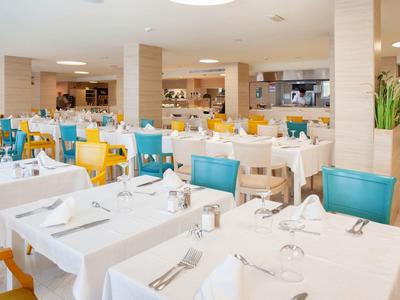 Comedor de hotel con mesas blancas, sillas coloridas y decoración moderna y luminosa.