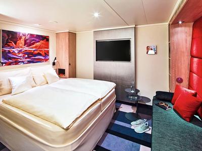 Nowoczesny pokój hotelowy z podwójnym łóżkiem, czerwonym kanapą i kolorową dekoracją.