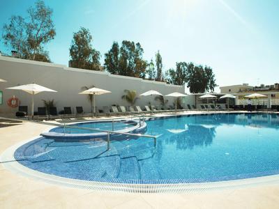 Piscine extérieure ronde avec parasols et chaises longues devant un bâtiment blanc par temps ensoleillé.