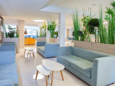 Jasna przestrzeń wypoczynkowa z nowoczesnymi sofami i zielonymi roślinami w hotelu.