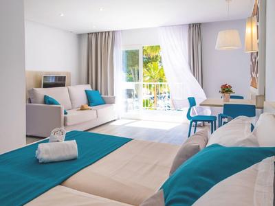 Helles Hotelzimmer mit Doppelbett, Balkon und moderner Einrichtung in Blau- und Weißtönen.