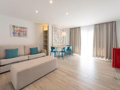 Helles Wohnzimmer mit grauem Sofa, türkisfarbenen Stühlen und großen Fenstern mit Vorhängen.