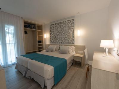 Helles Hotelzimmer mit Doppelbett, blauen Akzenten und Balkon mit Vorhängen.