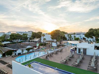 View of a hotel with pool, sun loungers, and white buildings at sunset.