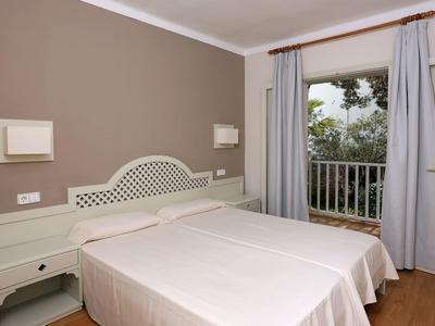 Schlichtes Doppelzimmer mit zwei Betten, weißem Nachttisch und Balkon mit Blick ins Grüne.