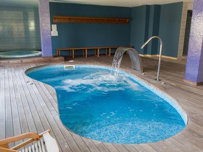 Innenbereich mit kleinem Pool, Holzdeck und Wasserfallattraktion im Hotelspa.