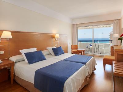Modernes Hotelzimmer mit Doppelbett, Holzmöbeln und Balkon mit Meerblick.