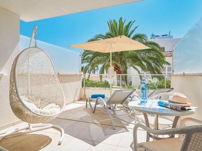 Terraza moderna con silla colgante, sombrilla y sillas, rodeada de palmeras.