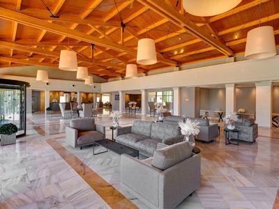 Amplia sala de estar de hotel con muebles modernos, sofás grises y techo con vigas de madera.