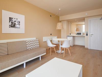 Área de estar abierta con cocina moderna, comedor y sofá en colores neutros.