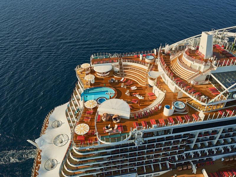 A cruise ship with multiple decks, swimming pools, and lounge areas sailing on the ocean.