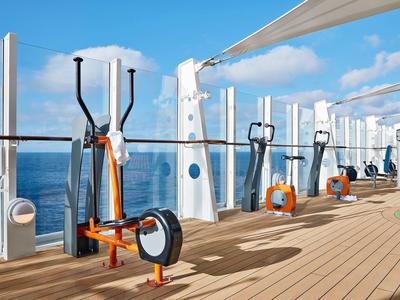 Terrazza di hotel con attrezzature fitness affacciata sul mare sotto un cielo sereno.