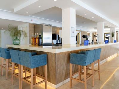 Bar dell'hotel moderno con sgabelli blu e bancone in legno chiaro.