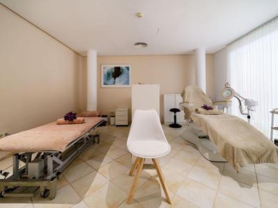 Lichte behandelkamer met twee behandelbedden, stoelen en natuurlijk licht door grote ramen.