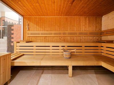 Intérieur d'un sauna avec des bancs en bois, un seau en bois et une fenêtre en verre vers l'extérieur.