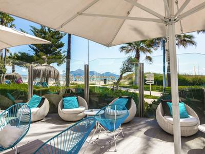 Terrasse avec sièges modernes et parasol, palmiers et vue sur la montagne en arrière-plan.