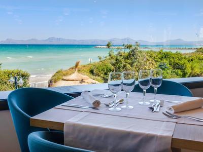 Une table dressée avec couverts et verres devant une grande fenêtre avec vue sur la mer.