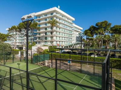 Modern hotel complex with tennis court and lush greenery under clear blue sky