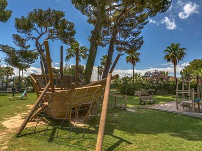 Aire de jeux avec une structure d'escalade en forme de bateau entourée d'arbres et d'espaces verts.