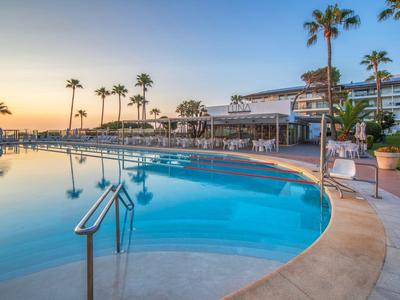 Piscine d'hôtel au coucher du soleil avec palmiers et restaurant adjacent