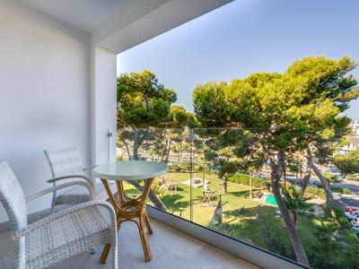 Balcon avec garde-corps en verre, deux chaises et petite table offrant une vue sur des arbres verts et un parc.