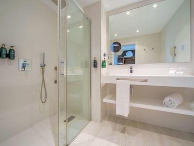 Salle de bain lumineuse avec douche à l'italienne, grand miroir et lavabo moderne.
