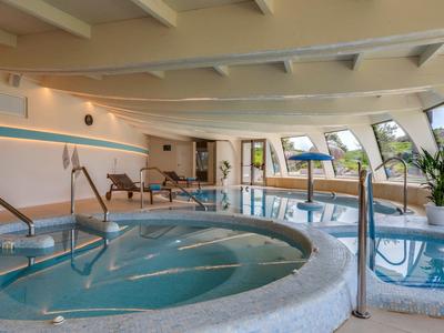 Piscine intérieure avec jacuzzi et sièges, murs clairs et grandes fenêtres