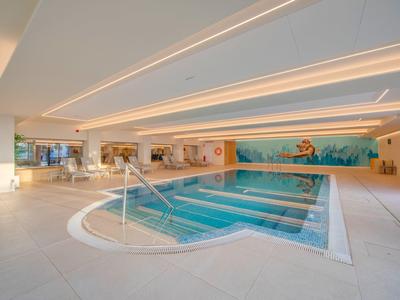 Piscine intérieure moderne avec eau claire, mur en mosaïque et éclairage lumineux.