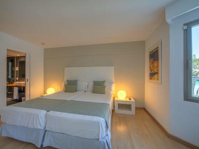 Chambre d'hôtel lumineuse et moderne avec lit double, tables de chevet et vue sur la piscine à travers la fenêtre.