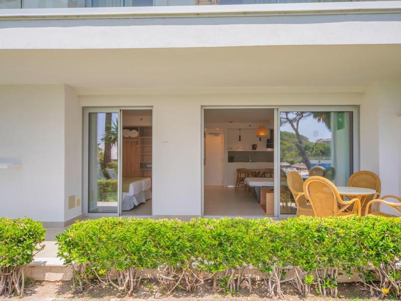 Porte-fenêtre donnant sur une chambre d'hôtel moderne avec mobilier extérieur et verdure soignée.