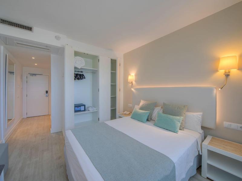 Chambre d'hôtel moderne avec lit double, murs clairs et éclairage indirect.