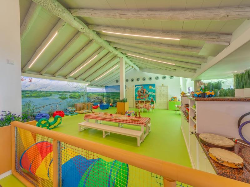 Salle de jeux intérieure lumineuse avec tapis vert, jouets colorés et meubles en bois sous toit incliné