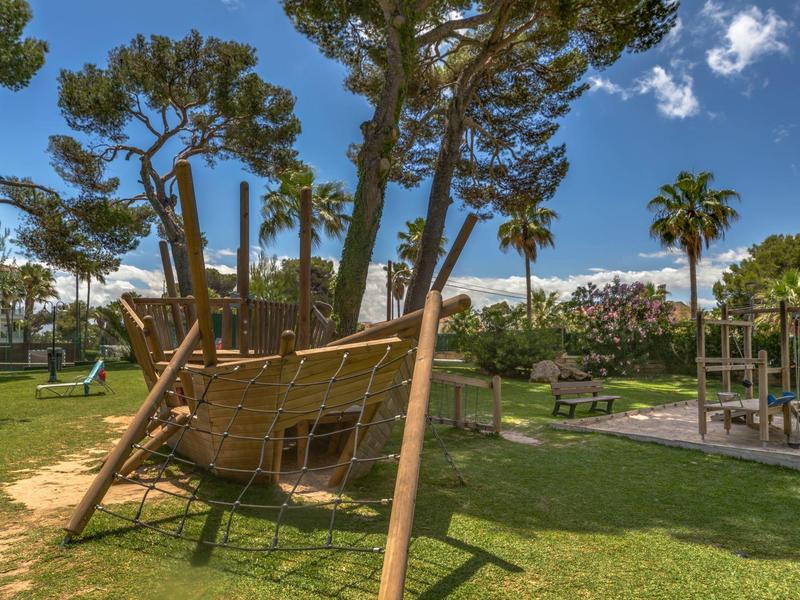 Aire de jeux avec une structure d'escalade en forme de bateau entourée d'arbres et d'espaces verts.