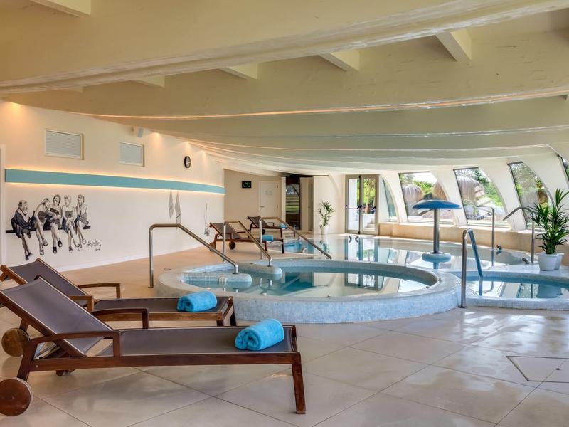 Espace spa intérieur avec jacuzzi, chaises longues et grandes fenêtres.