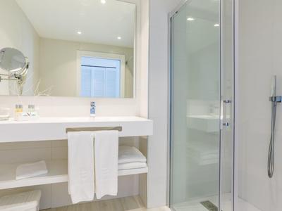 Weißes Badezimmer mit Waschbecken, Spiegel, Handtüchern und einer Duschkabine rechts.