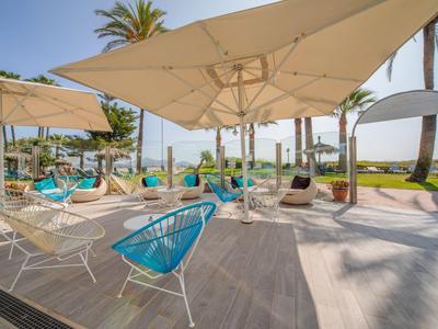 Modern outdoor area with chairs, umbrellas, and palm trees near a hotel