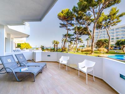 Balkon mit Liegestühlen und Stühlen neben einem Pool mit Blick auf Bäume und Hotelgebäude.