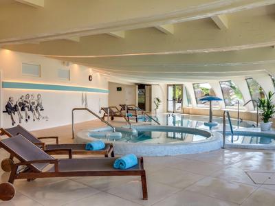 Innenbereich eines Wellnessbereichs mit Whirlpool, Liegestühlen und großen Fenstern.